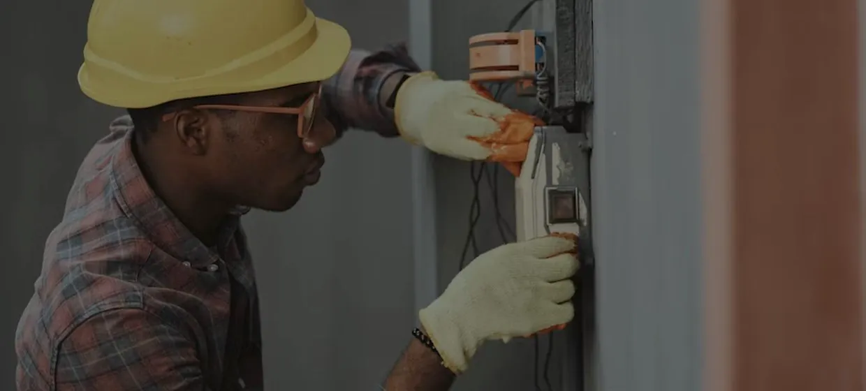 Electrician in a hard hat working on a wall-mounted installation