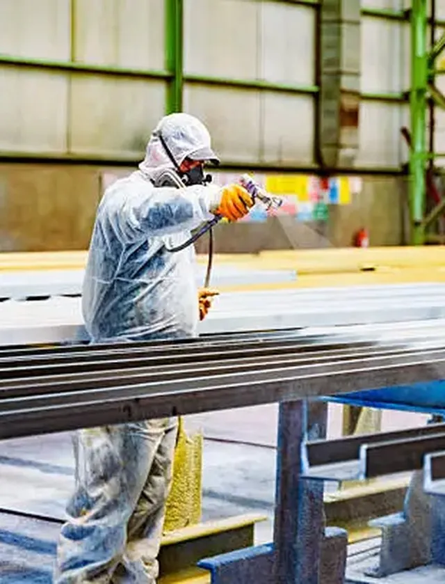Spray painter in protective overalls coating structural steel