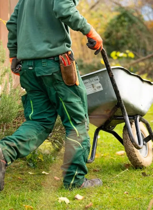 Maintenance worker moving a wheelbarrow across the grounds of a property